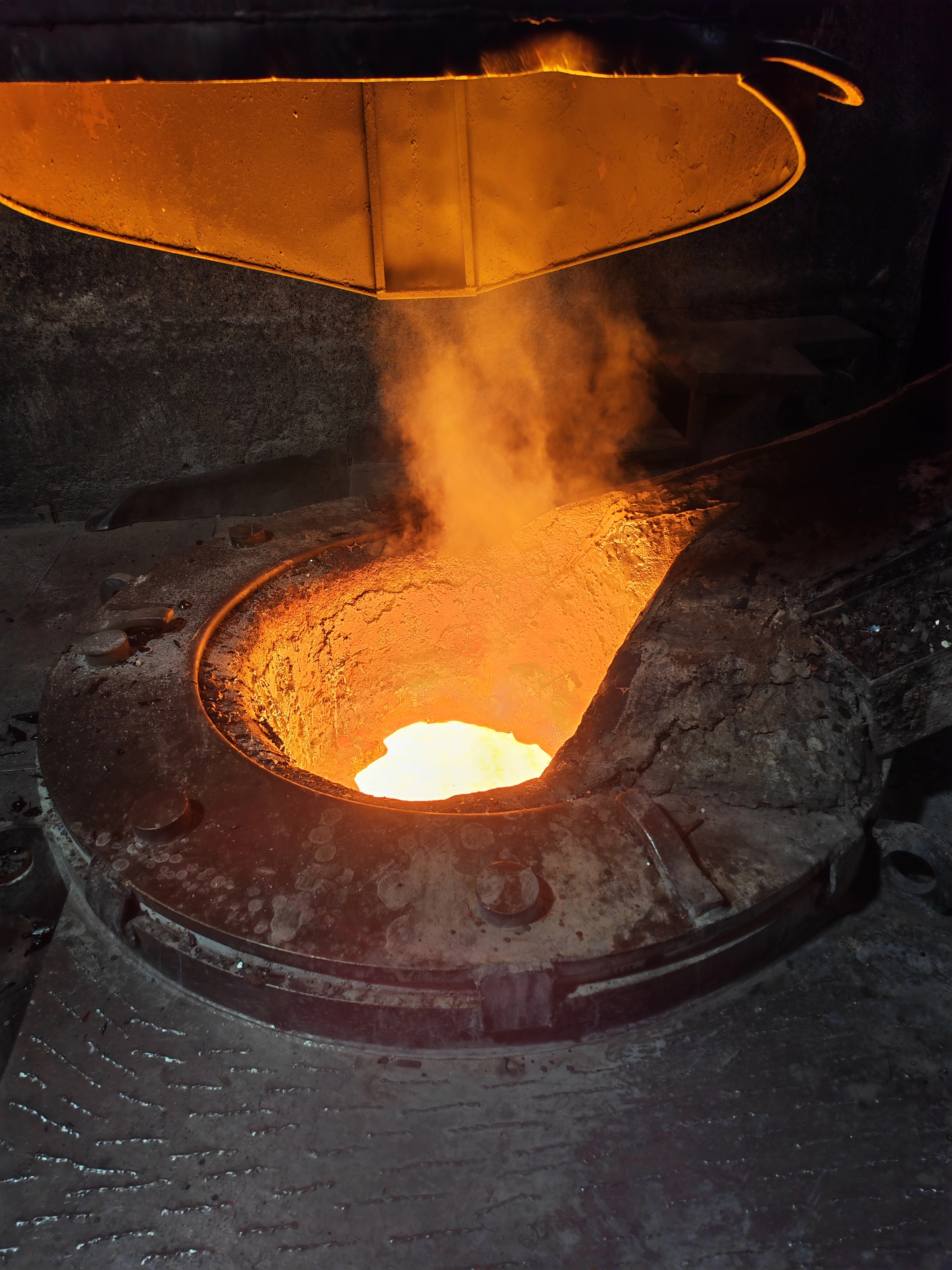 IMG_20251104_165903 Heißer Schmelzofen mit flüssigem Metall und aufsteigendem Dampf in einer dunklen industriellen Umgebung.