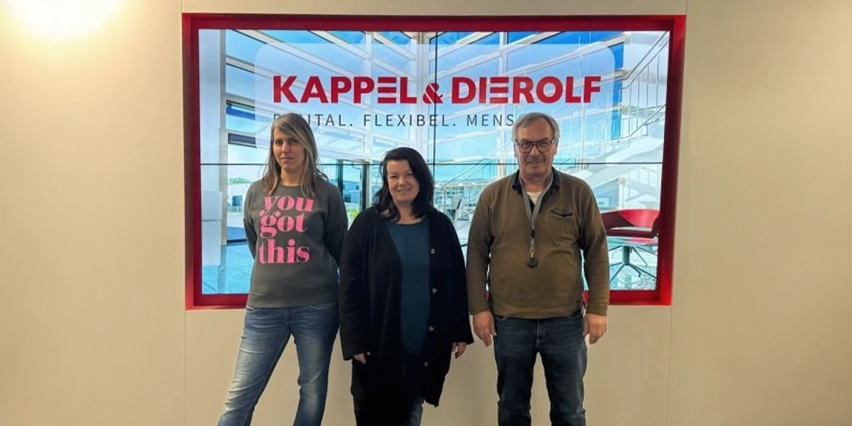 Drei Personen vor einem Bildschirm mit Kappel & Dierolf Logo, in einem modernen Büro.