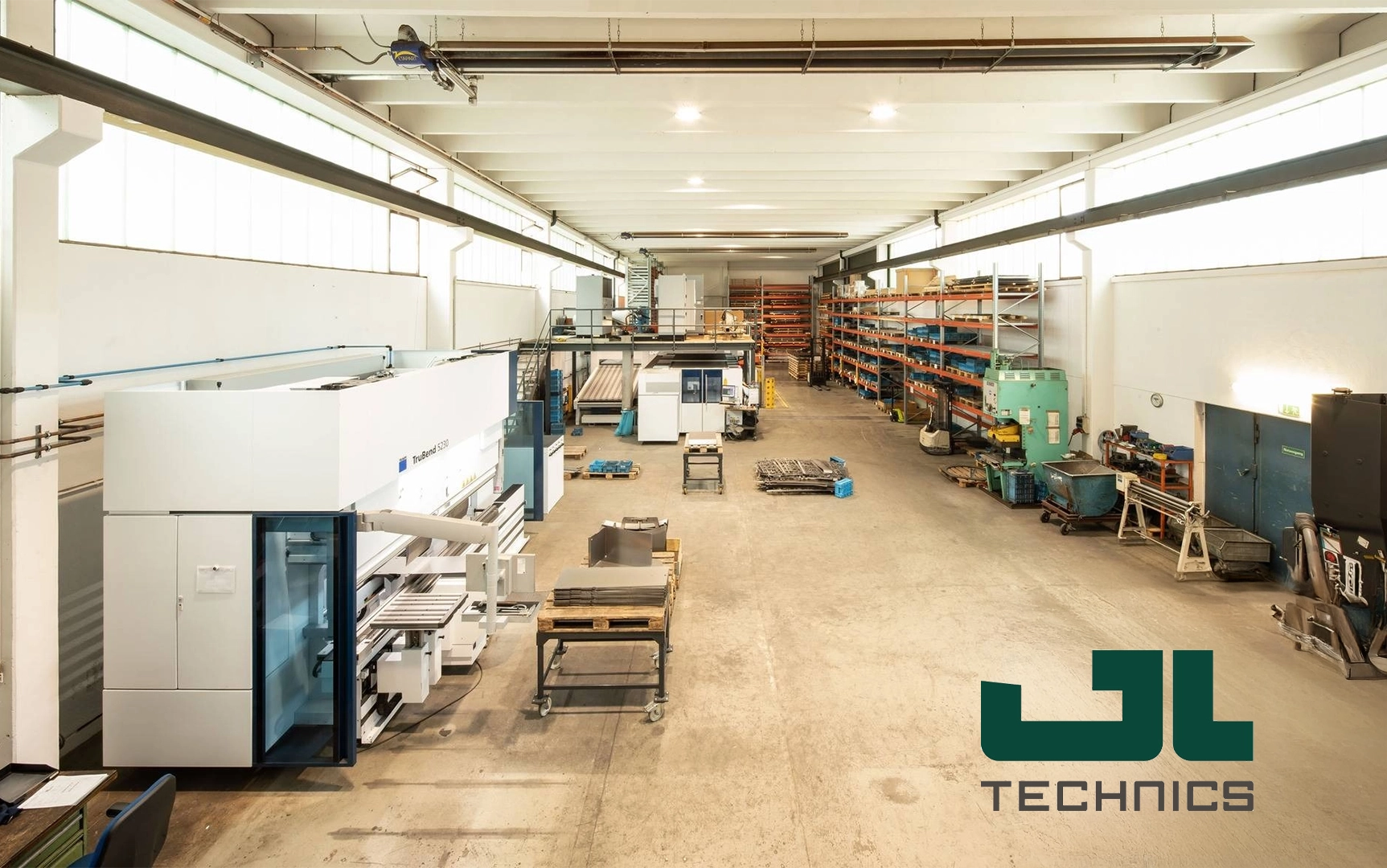 Kappel-Dierolf_Cases_GL-GmbH Große, helle Werkshalle mit Maschinen, Regalen und Materialien. Logo „JL Technics“ im Vordergrund.