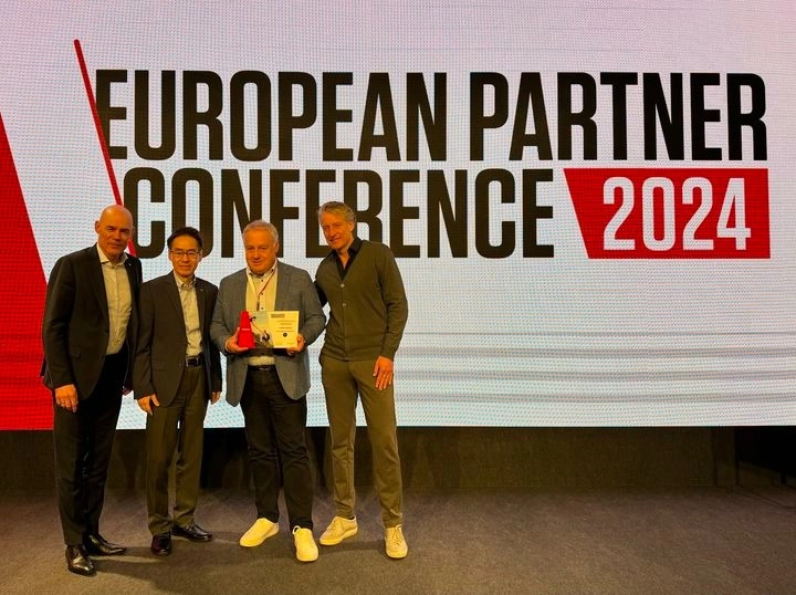 Vier Personen posieren vor einem Schild mit der Aufschrift European Partner Conference 2024 auf einer Bühne.