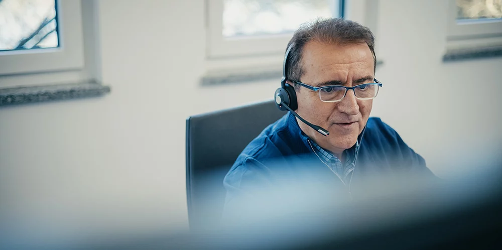 Kappel_Kompetenzen_Support Ein Mann mit Headset sitzt an einem Schreibtisch und arbeitet konzentriert am Computer in einem modernen Büro.