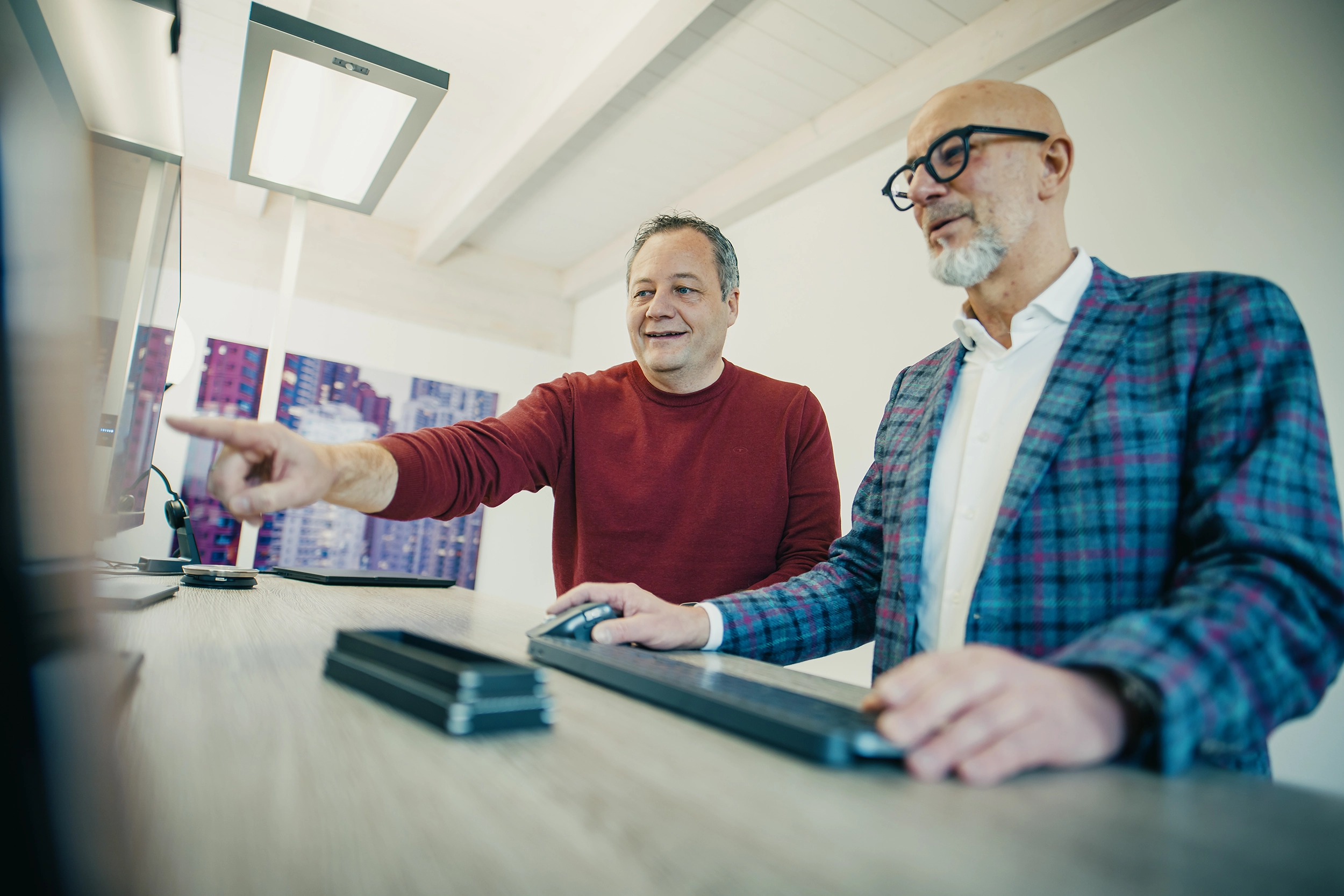 Zwei Männer arbeiten am Computer im Büro, einer zeigt auf den Bildschirm, der andere bewegt die Maus.