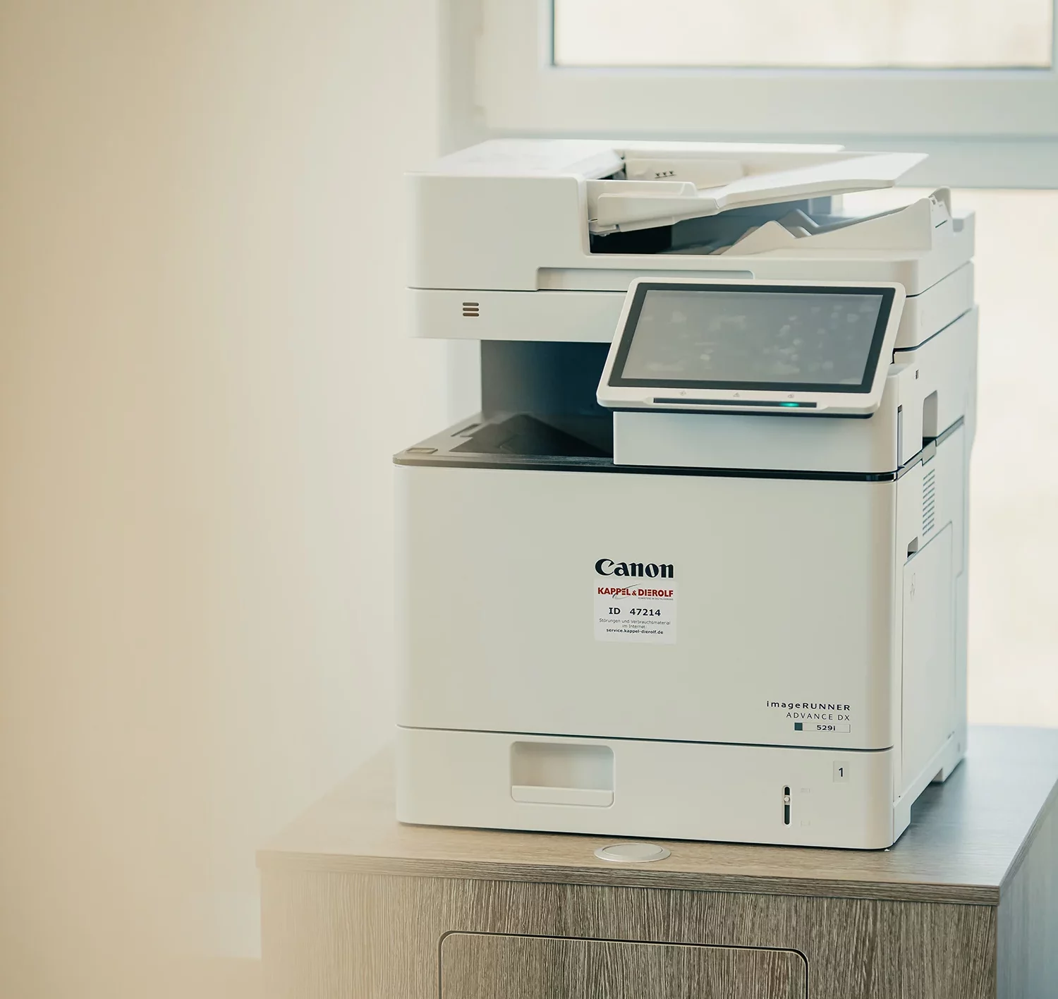 Kappel_Druckervielfalt Ein weißer Canon-Multifunktionsdrucker steht auf einem Holztisch vor einem Fenster in einem Büro.