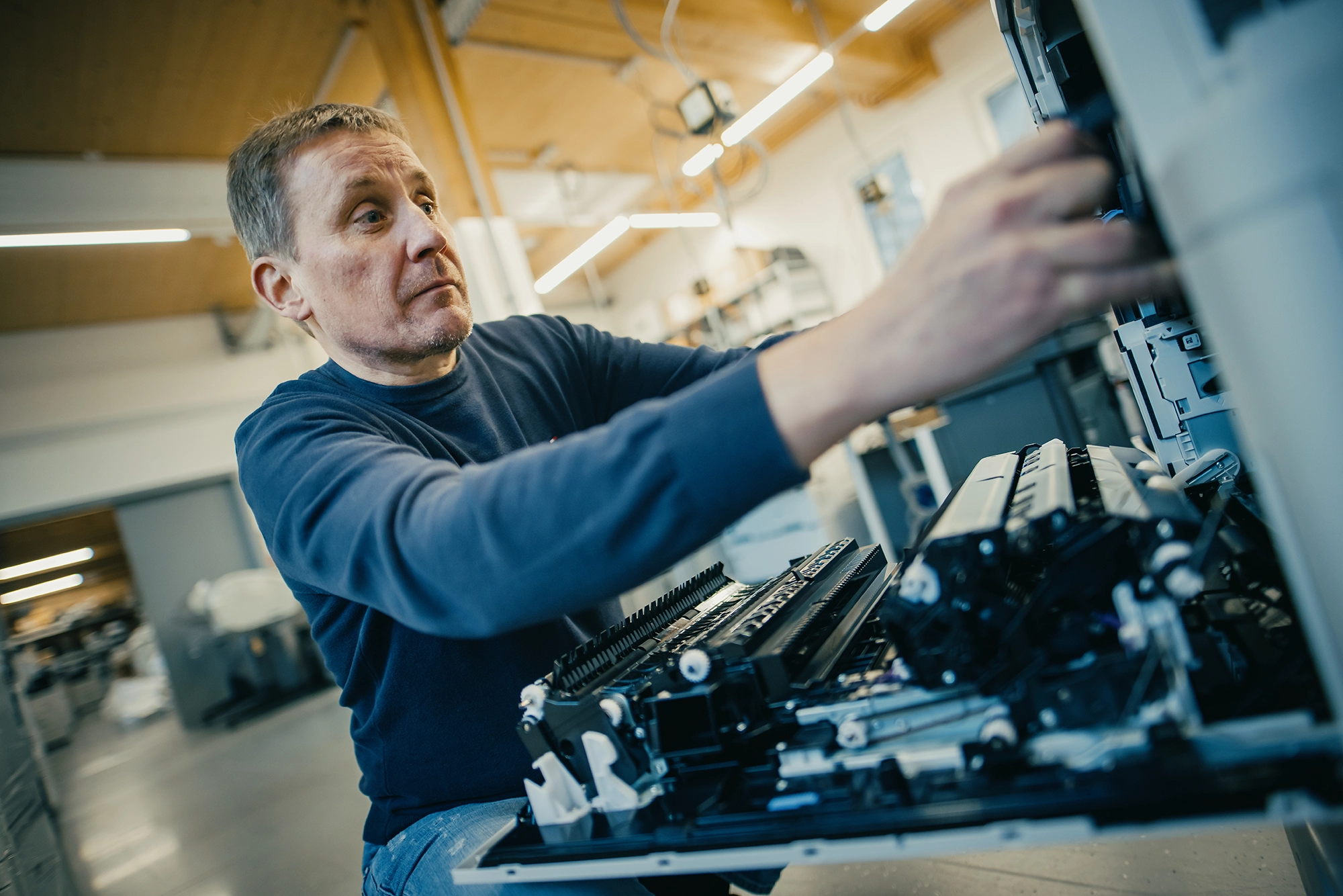 Mann in Werkstatt repariert Kopierer, konzentriert arbeitend. Helle, moderne Umgebung mit industriellen Elementen.