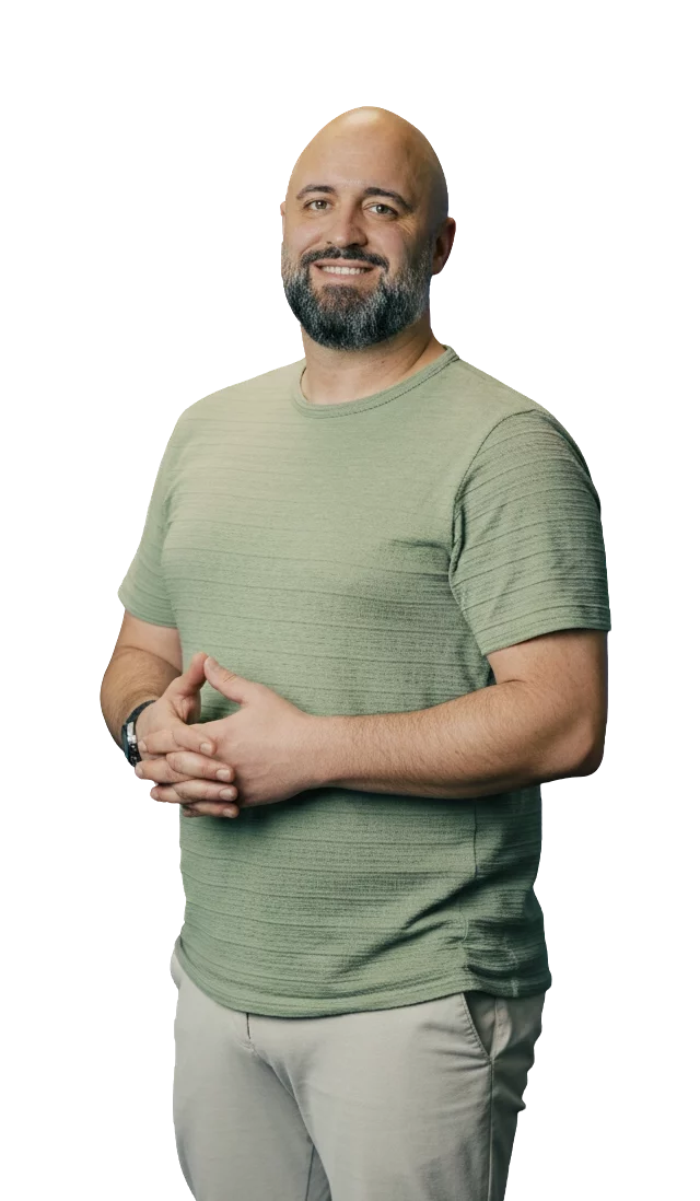 Kappel_Mäder Ein Mann mit Bart in einem grünen T-Shirt steht lächelnd mit verschränkten Händen vor einem neutralen Hintergrund.