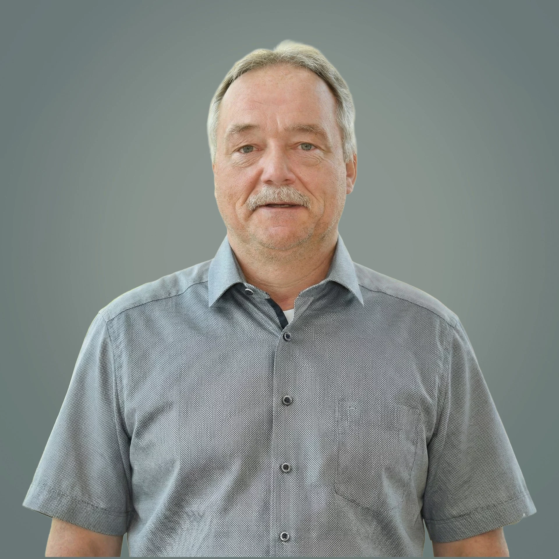 Ein Mann mittleren Alters in grauem Hemd steht vor grauem Hintergrund und blickt in die Kamera.