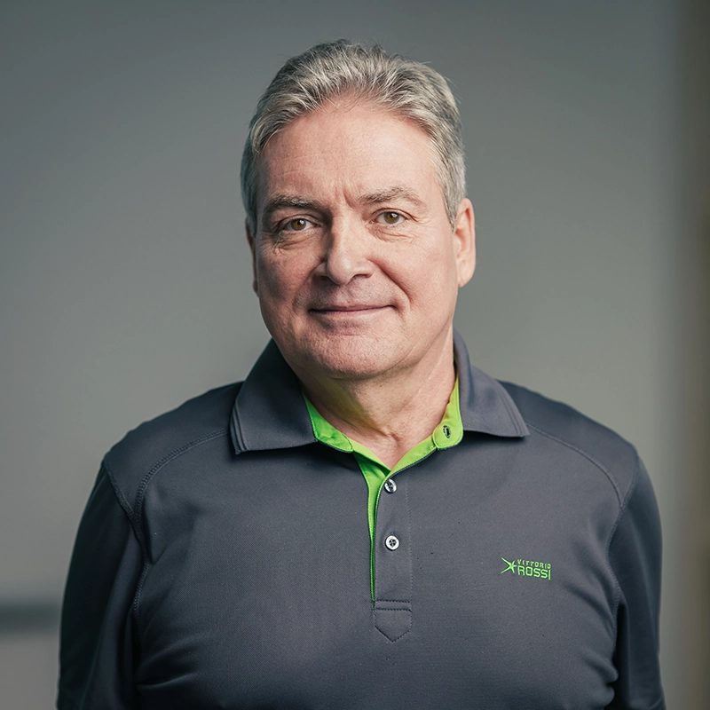 Ein Mann in einem grauen Poloshirt mit grünem Kragen steht vor einem neutralen Hintergrund.