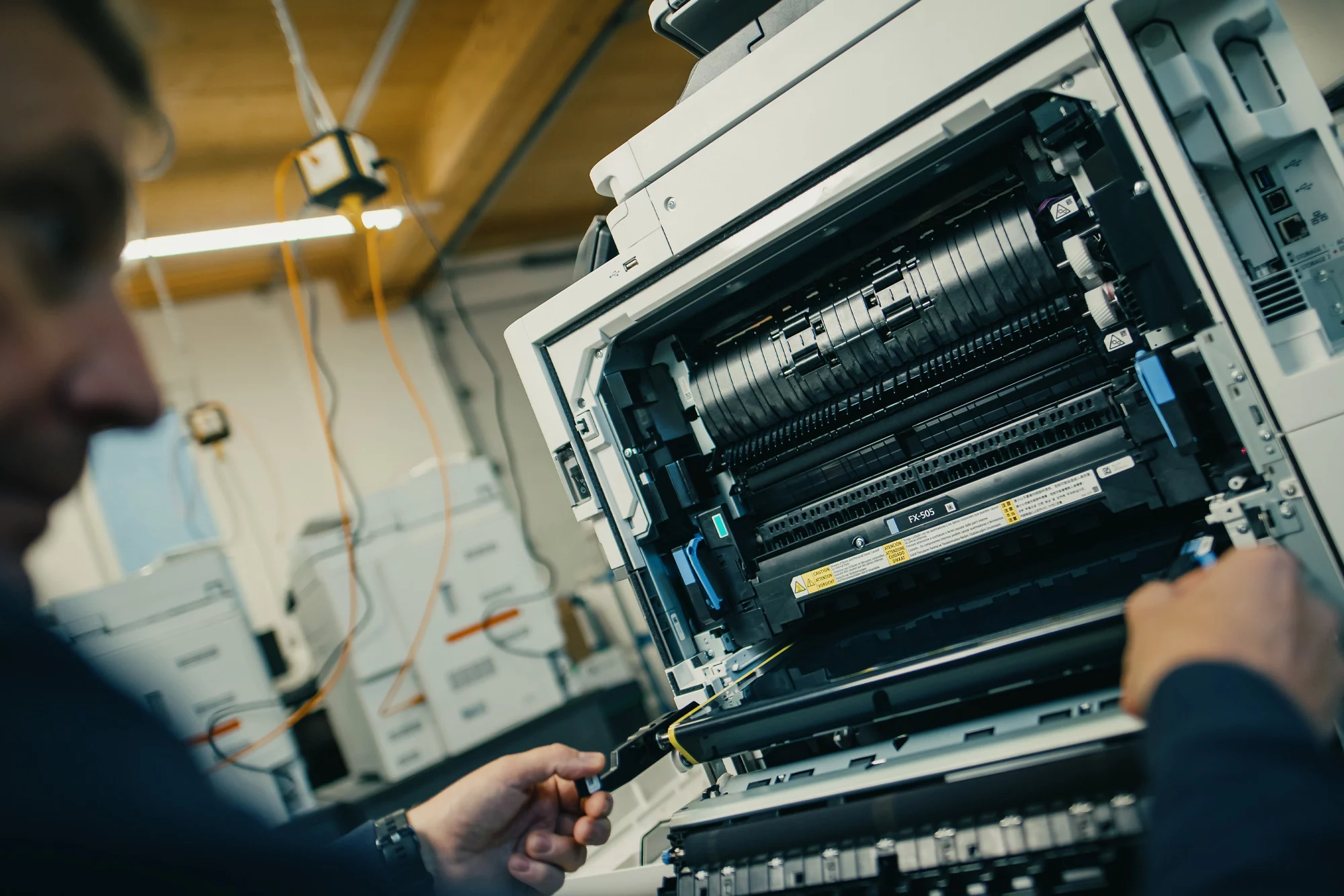 Techniker repariert geöffneten Kopierer in einem Büro, Nahaufnahme der internen Mechanik und Werkzeuge.