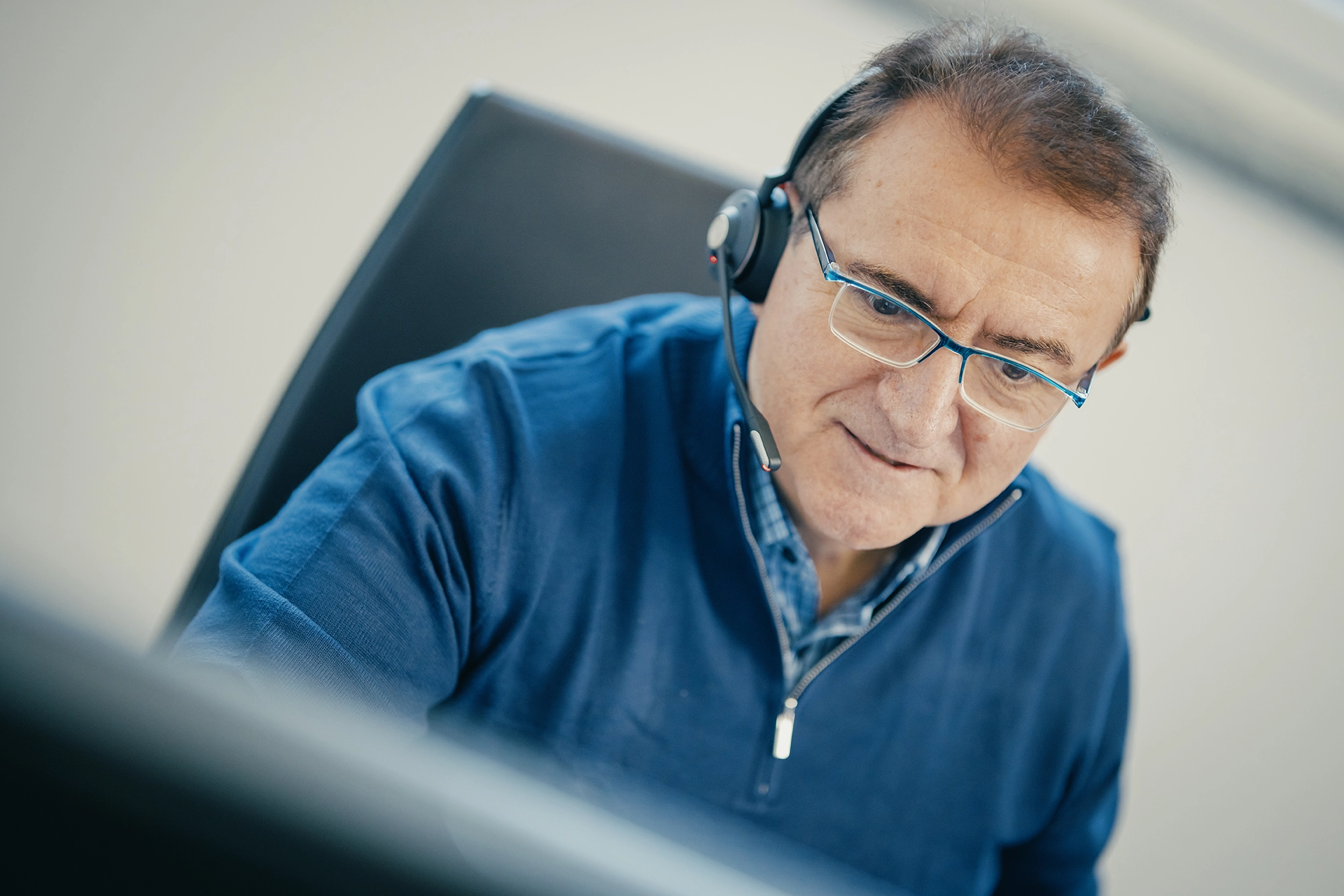 Älterer Mann mit Brille und Headset arbeitet konzentriert am Computer.