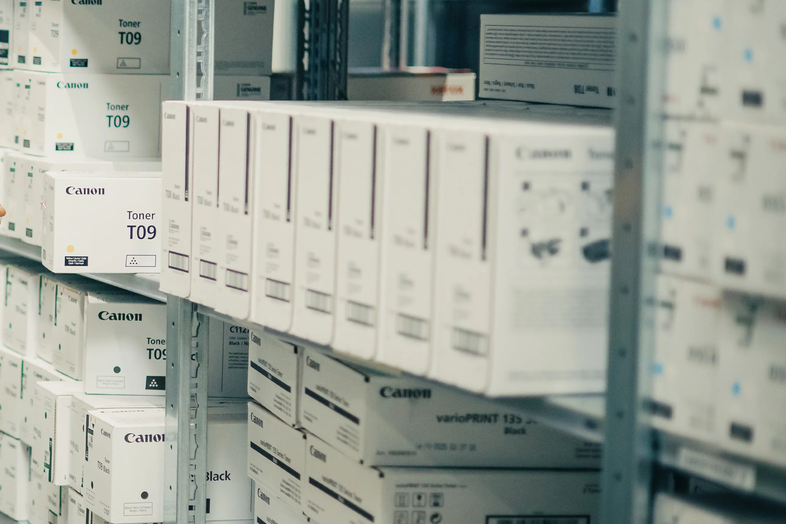 Mann im Lager scannt Kartons mit Handscanner, umgeben von Regalen mit Produkten.