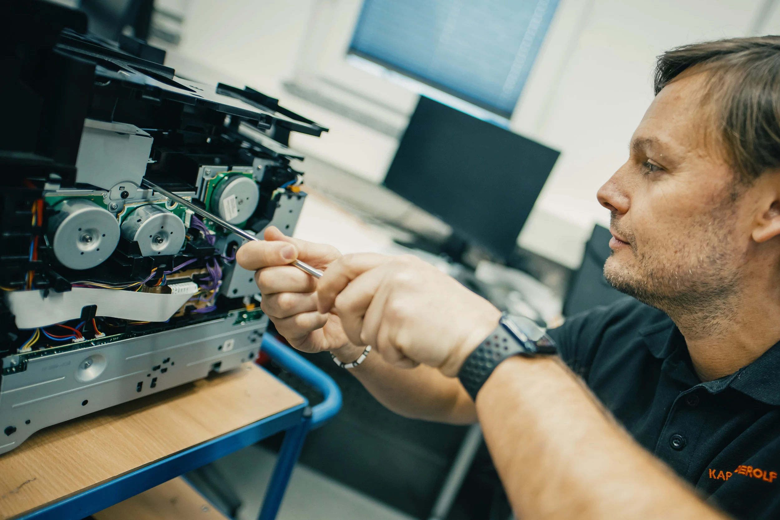 Mann in Lager, scannt Canon-Toner-Box mit Scanner in der Hand; umgeben von Regalen mit Kartons.
