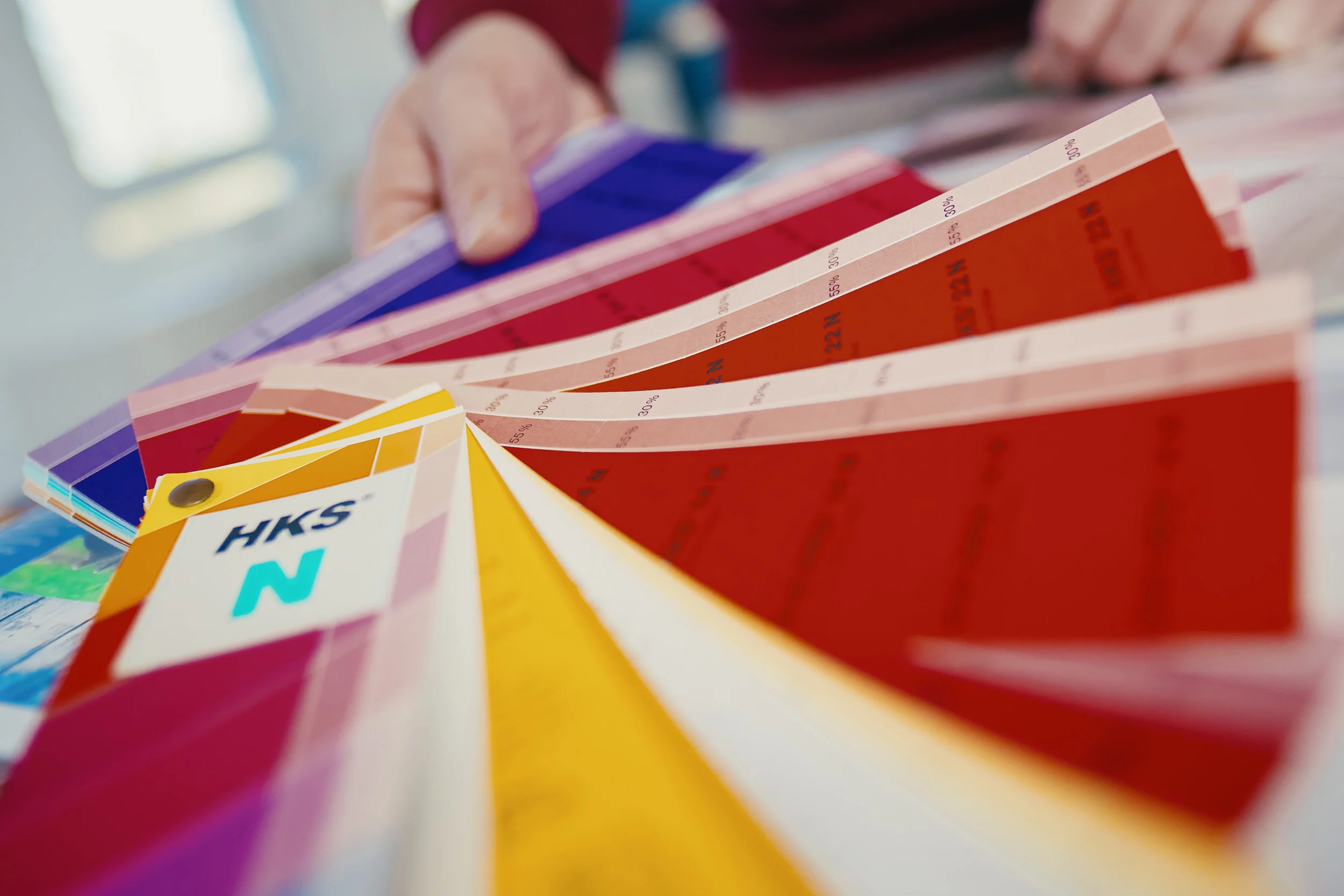Zwei Männer begutachten Farbdrucke in einem modernen Büro mit Druckgeräten im Hintergrund.