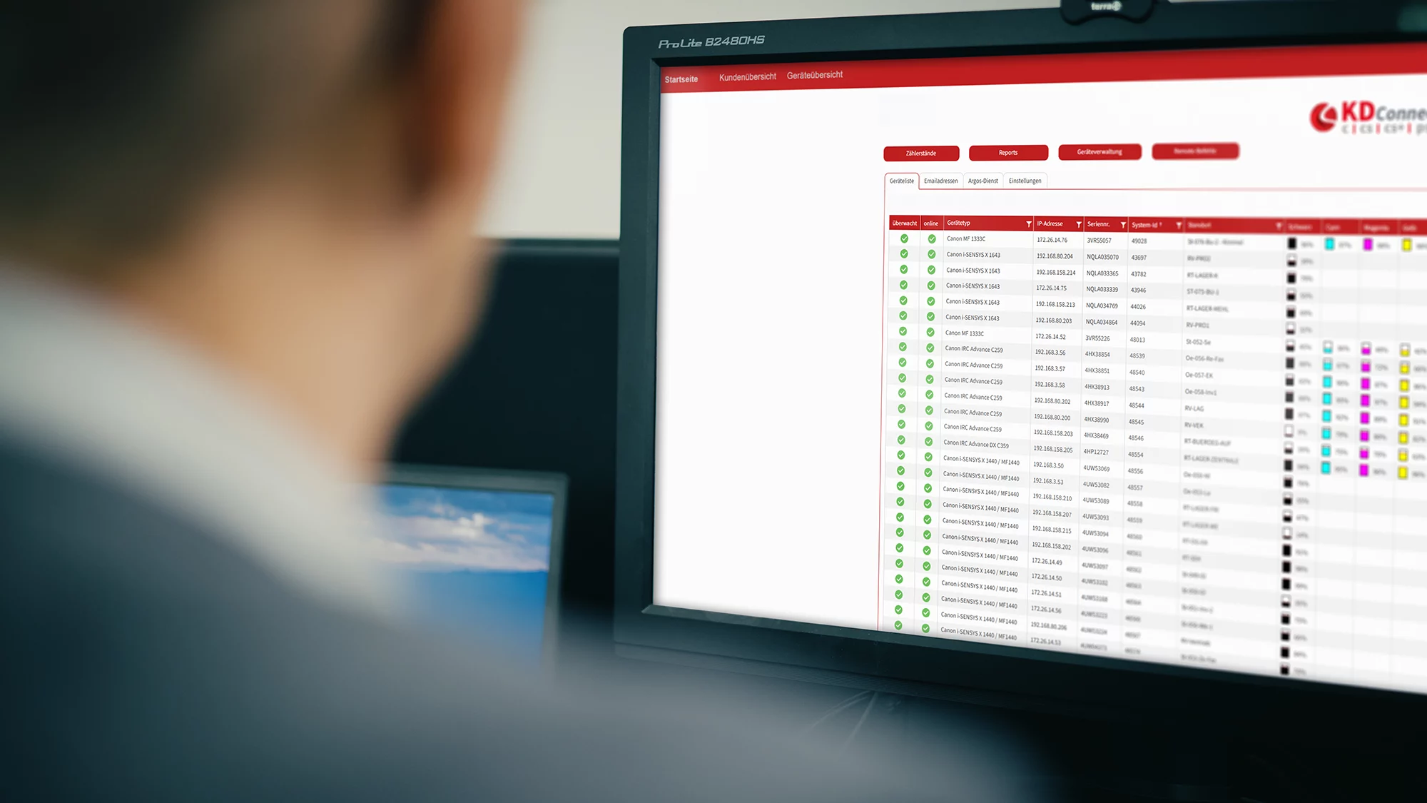 Mann betrachtet Bildschirm mit Softwareübersicht zur Geräteverwaltung, einschließlich Statusanzeigen für Drucker.
