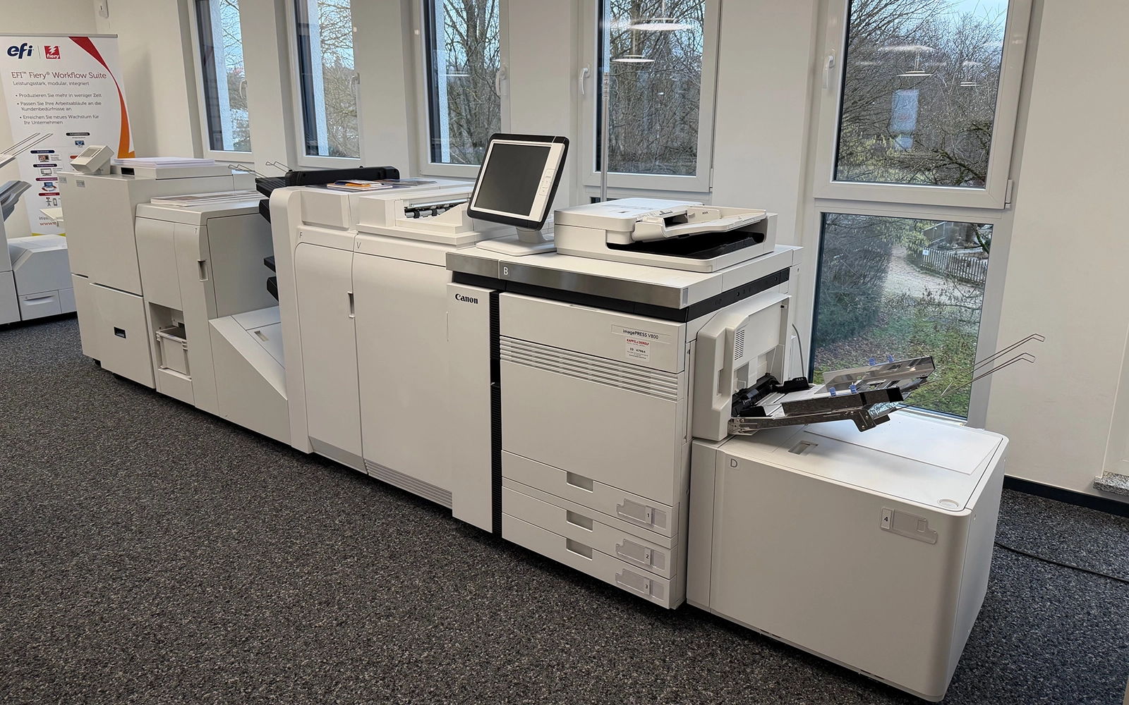 Canon Drucksystem in einem modernen Büro, ausgestattet mit Monitor und verschiedenen Drucker- und Finisher-Einheiten.
