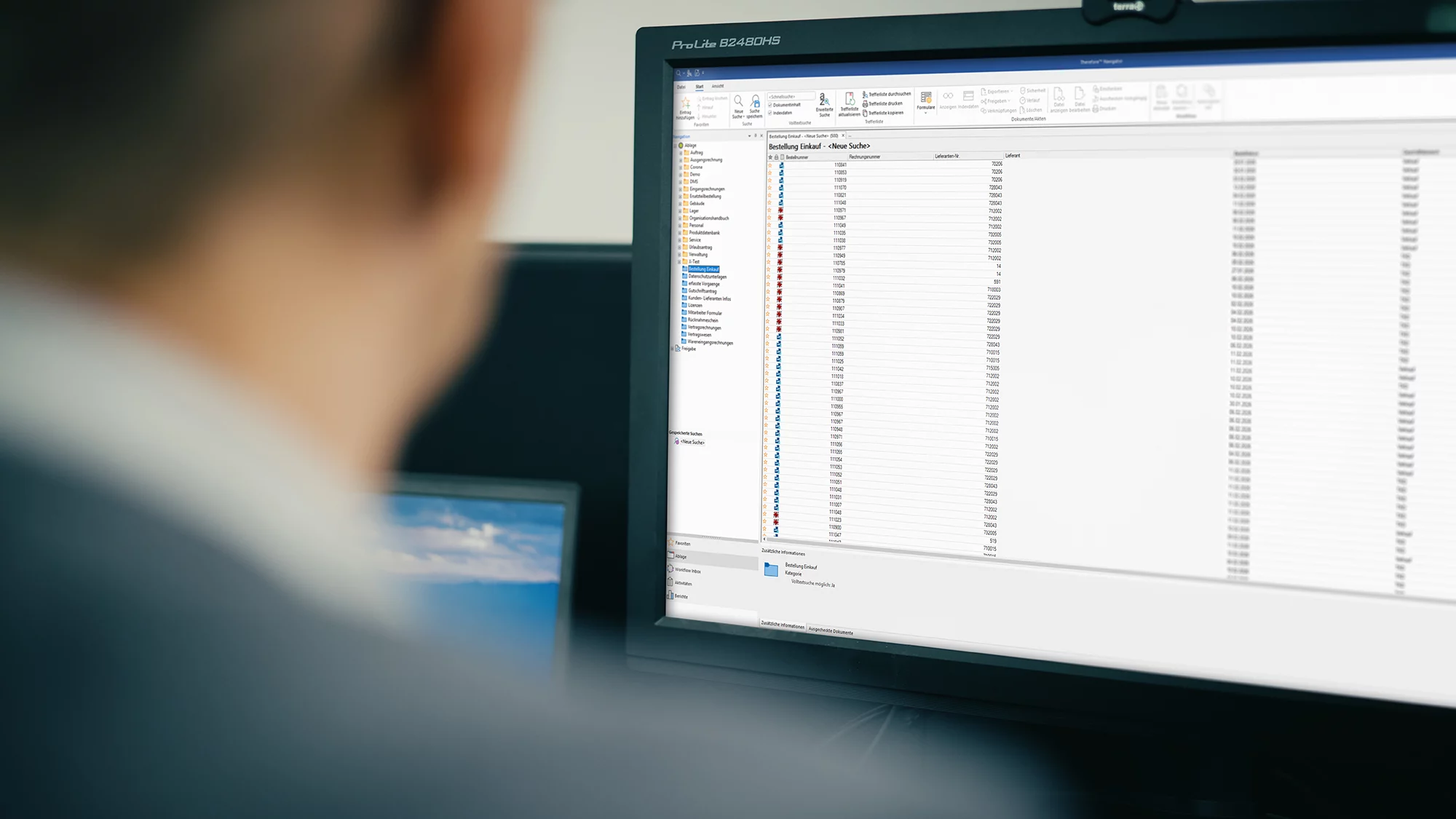 Mann betrachtet einen Computerbildschirm mit einer Tabelle von Bestellungen und Lieferinformationen im Büro.